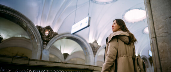 A young woman stands at a beautiful old subway station.