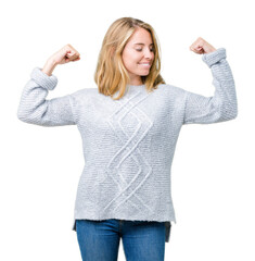 Beautiful young woman wearing winter sweater over isolated background showing arms muscles smiling proud. Fitness concept.