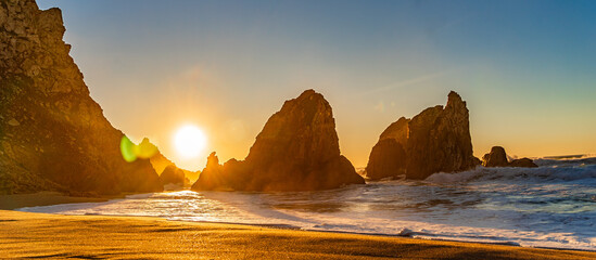 Sunset on the Portugal Ursa Beach, Praia da Ursa, 
the westernmost beach at atlantic coast of Atlantic Ocean with sand and sunset sun waves and foam at sand of coastline picturesque landscape panorama - obrazy, fototapety, plakaty