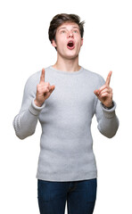 Young handsome man wearing winter sweater over isolated background amazed and surprised looking up and pointing with fingers and raised arms.