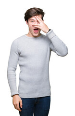 Young handsome man wearing winter sweater over isolated background peeking in shock covering face and eyes with hand, looking through fingers with embarrassed expression.