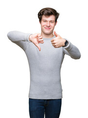 Young handsome man wearing winter sweater over isolated background Doing thumbs up and down, disagreement and agreement expression. Crazy conflict