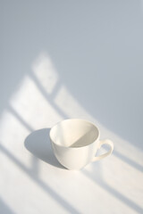 Light and shadow fall from the window onto a white cup.