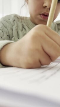 Close-up of girl writing her homework at home and using the eraser