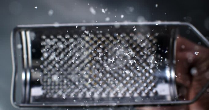 Super slow motion macro of stellar chef grating traditional parmesan cheese with steel grater on the dish close up and pieces of cheese fall at 1000 fps for preparing pasta.