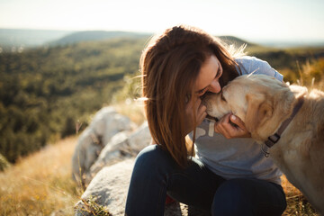 young woman and old labrador dog sharing an intimate moment sitting on a hill