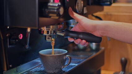 Freshly brewed coffee flows in a thin stream from the coffee machine into a beautiful gray cup, the barista brewed a cup of coffee for the visitor, an invigorating drink in a coffee shop.