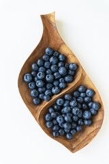 Leaf-shaped wooden bowl filled with fresh blueberries. Blueberries are ripe and have a bright dark blue color.