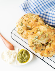 Fresh pumpkin seed bread with pesto and cream cheese on wire rack, blue checkered cloth background.