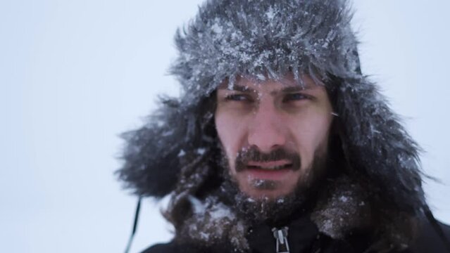 a bearded man in earflaps and snow