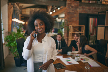 Portrait of smiling African-American woman, student in official clothes with talking on phone while preparing for exam in public library. Selective focus. Concept of business, study, co-working space. - obrazy, fototapety, plakaty