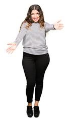 Young beautiful woman wearing stripes sweater looking at the camera smiling with open arms for hug. Cheerful expression embracing happiness.