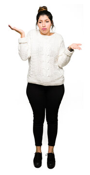 Young beautiful woman wearing winter sweater clueless and confused expression with arms and hands raised. Doubt concept.