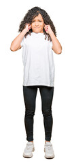 Fototapeta premium Young beautiful woman with curly hair wearing white t-shirt covering ears with fingers with annoyed expression for the noise of loud music. Deaf concept.