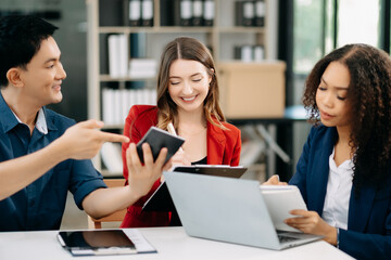 Obraz premium Happy businesspeople while collaborating on a new project in an office. Group of diverse businesspeople using a laptop and tablet .