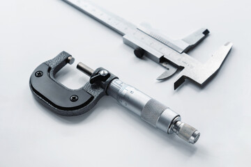Close-up of a mechanical micrometer and caliper on a light background.