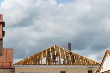 A new wooden roof structure lining a house in the city. Industrial roofing system with wooden beams, ceilings and tiles. Roofing works.