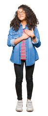 Young beautiful woman with curly hair wearing glasses smiling with hands on chest with closed eyes and grateful gesture on face. Health concept.