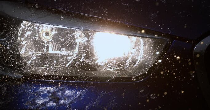 Super slow motion macro of splashing rain water drops are falling on turned on car headlights while raining at night. 1000 fps