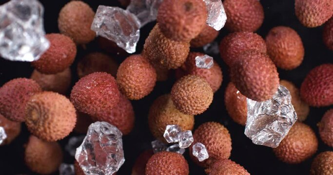 Super slow motion of fresh bio organic pieces are flying lychee fruits and shiny pure water ice cubes at 1000 fps isolated on black background
