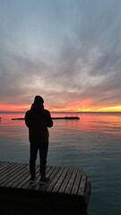 uomo guarda il tramonto sul pontile del lago