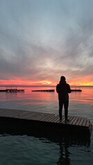 uomo guarda il tramonto sul pontile del lago