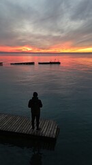 Fototapeta premium uomo guarda il tramonto sul pontile del lago