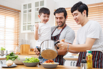 Happy cheerful LGBTQ couple cooking a food together in kitchen.