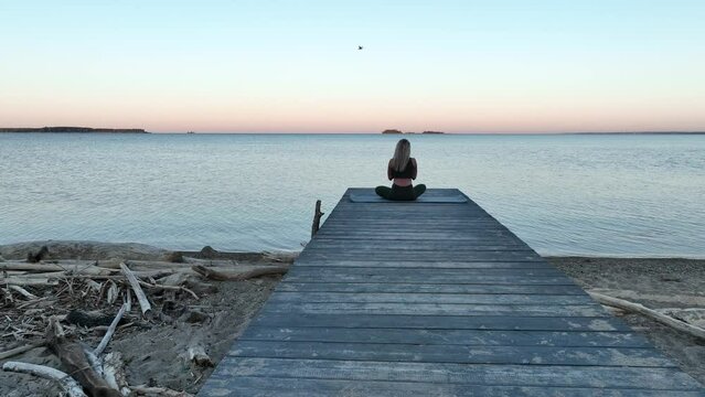 The young woman does meditation on the wood pier by the sea. Morning, dawn. Aerial view	
