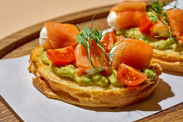 Bruschetta with bacon and guacamole on a wooden plate on a light background