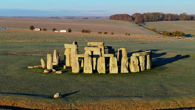 Aerial shot circling around Stonehenge in bright low sunlight casting long shadows