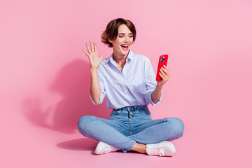 Full body photo of excited pretty lady sit floor hold smart phone take selfie record video arm wave hi isolated on pink color background