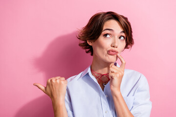 Portrait of minded pretty girl touch chin look direct finger empty space ad blank isolated on pink...