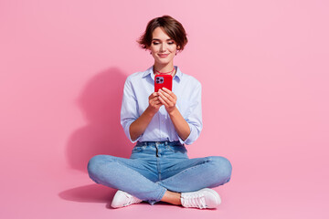 Full size photo of gorgeous girl sit floor use smart phone texting eshopping isolated on pink color...