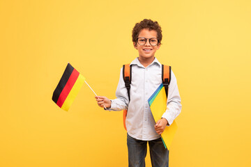 Grinning boy with German flag and school folders, yellow background