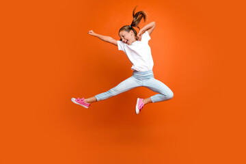 Full body portrait of energetic sporty girl jumping flying leg kick fight isolated on orange color...