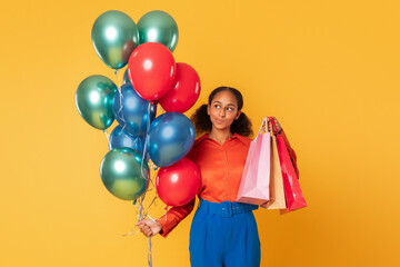 Fototapeta na wymiar african teenager girl holds shopping bags and balloons, yellow backdrop