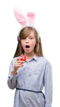 Young blonde child wearing easter bunny ears scared in shock with a surprise face, afraid and excited with fear expression