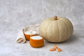 Pumpkin orange mousse in glasses next to round pumpkin fruit on gray background. Copy space.