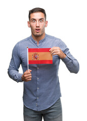 Handsome young man holding a flag of Spain scared in shock with a surprise face, afraid and excited with fear expression