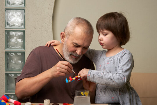 Preschool Development. A grandfather and granddaughter share a hobby together. They paint a toy made of clay.