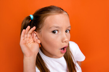 Portrait of impressed schoolkid arm near ear open mouth listen eavesdrop isolated on orange color background
