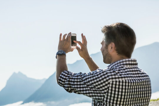 man taking a picture with oldschool cellphone in the mountains