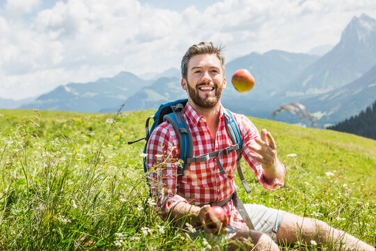 Portait junger Mann mit Apfel im Karohemd in den Bergen, &Ouml;sterreich