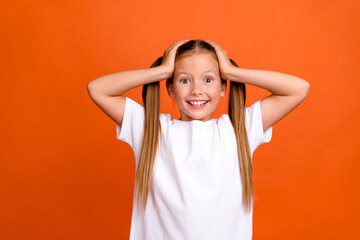 Photo portrait of pretty small girl hands touch head excited shocked wear trendy white outfit isolated on orange color background