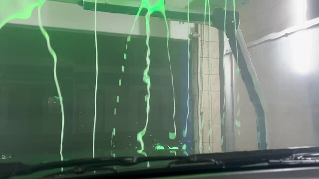 Robot car wash. Operation of an automatic wash system. A colorful short video of soaping a car at a car wash. Soap solution. Texture of white foam detergent through car glass.