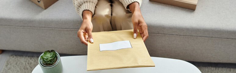 cropped view of young african american woman holding paper post packet above table, banner