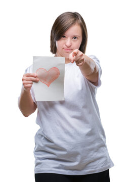 Young adult woman with down syndrome holding red heart card over isolated background pointing with finger to the camera and to you, hand sign, positive and confident gesture from the front