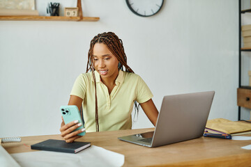 attractive jolly african american female seller looking at her smartphone during work, delivery