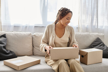 good looking jolly african american woman sitting on sofa and preparing to open cardboard box